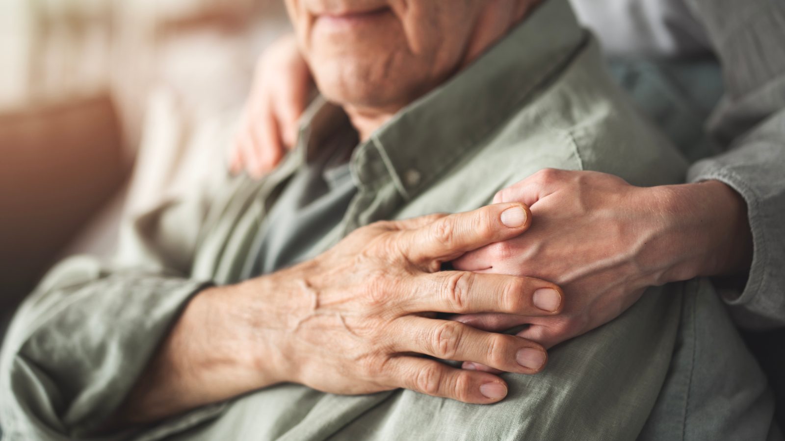 Elderly man holding the hand of a loved one resting on his shoulder