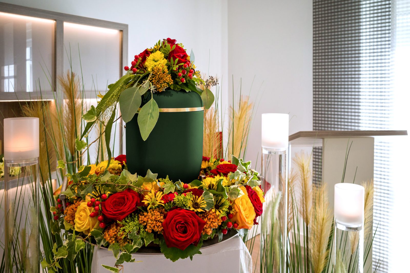 Green cremation urn surrounded by red and yellow flowers at a memorial service