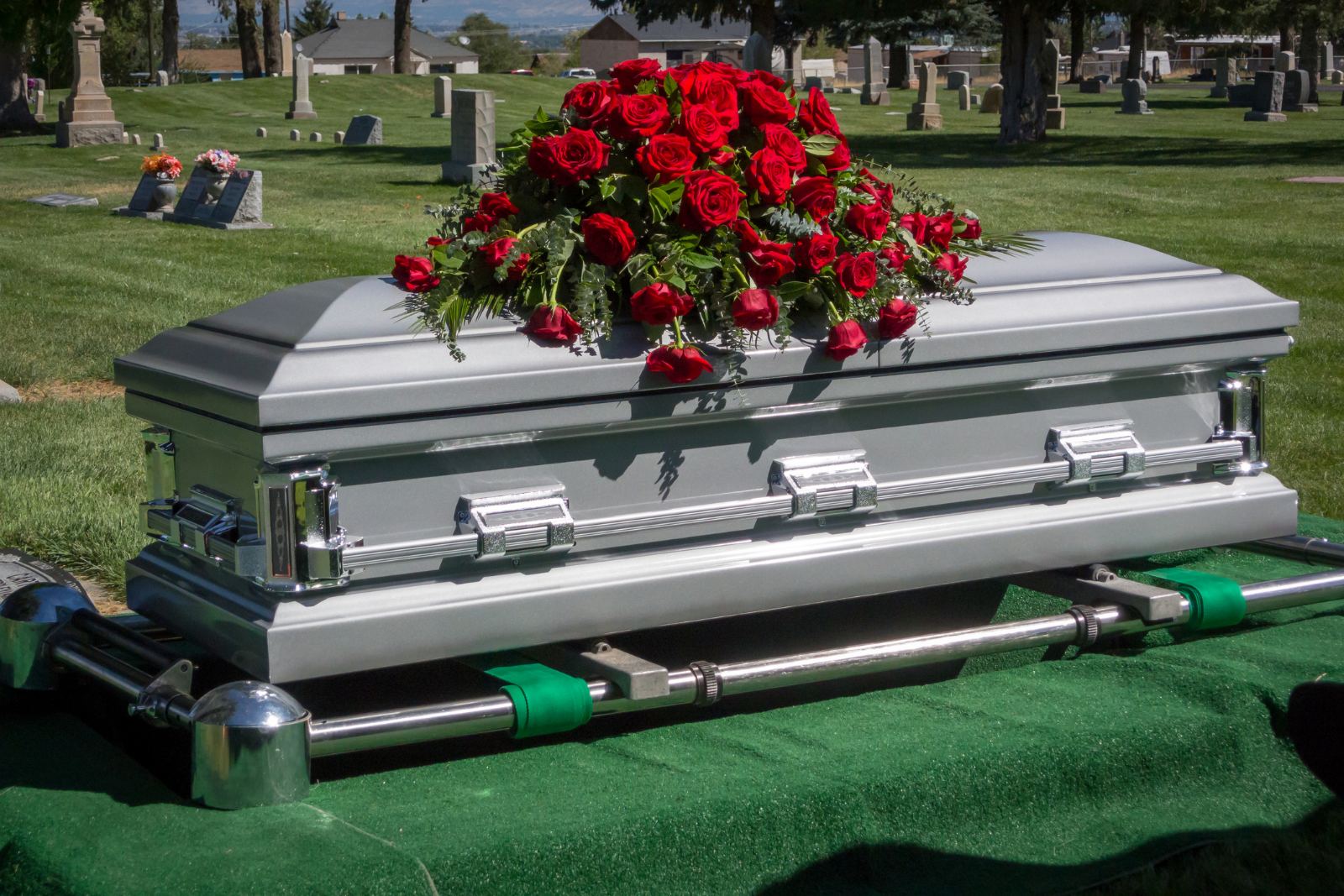 Silver casket topped with a spray of red roses at a graveside service in a cemetery